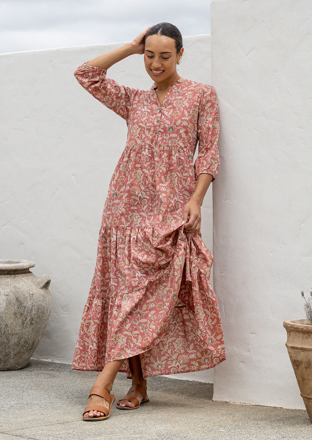 Woman standing in rose pink based 100% cotton flowy tiered maxi dress with 3/4 sleeves, buttoned bodice and pockets 