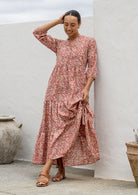 Woman standing in rose pink based 100% cotton flowy tiered maxi dress with 3/4 sleeves, buttoned bodice and pockets 