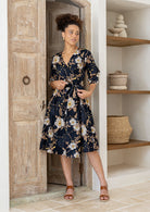 Model posing in over the knee length wrap dress with flowing skirt and formation of V neckline.