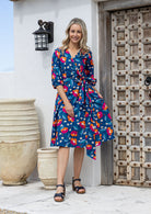 Model wears a royal blue based floral printed cotton wrap dress with V-neckline, 3/4 sleeves, a wide waist-tie and pockets