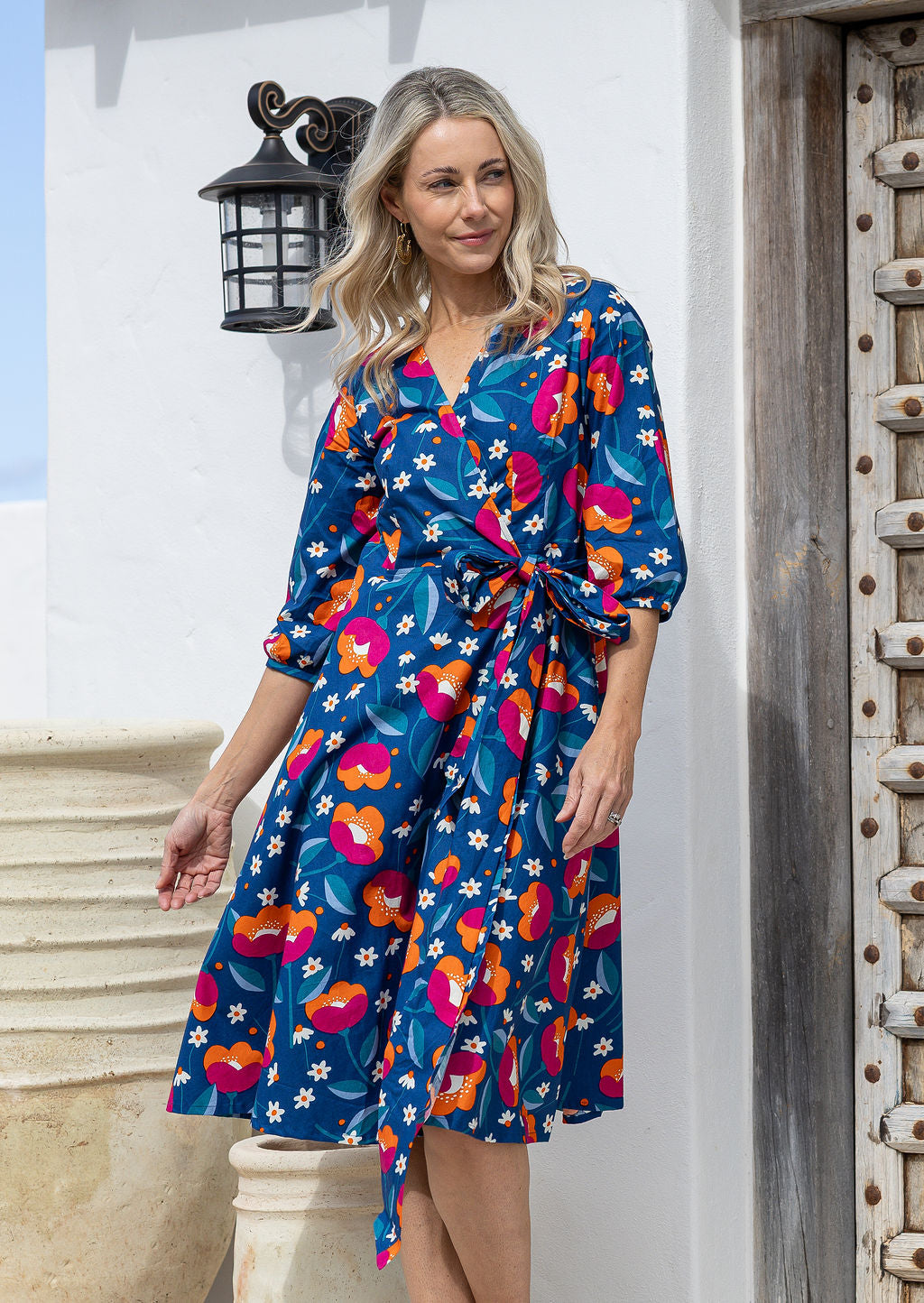 Model posing in over the knee length wrap dress with flowing skirt and formation of V neckline.