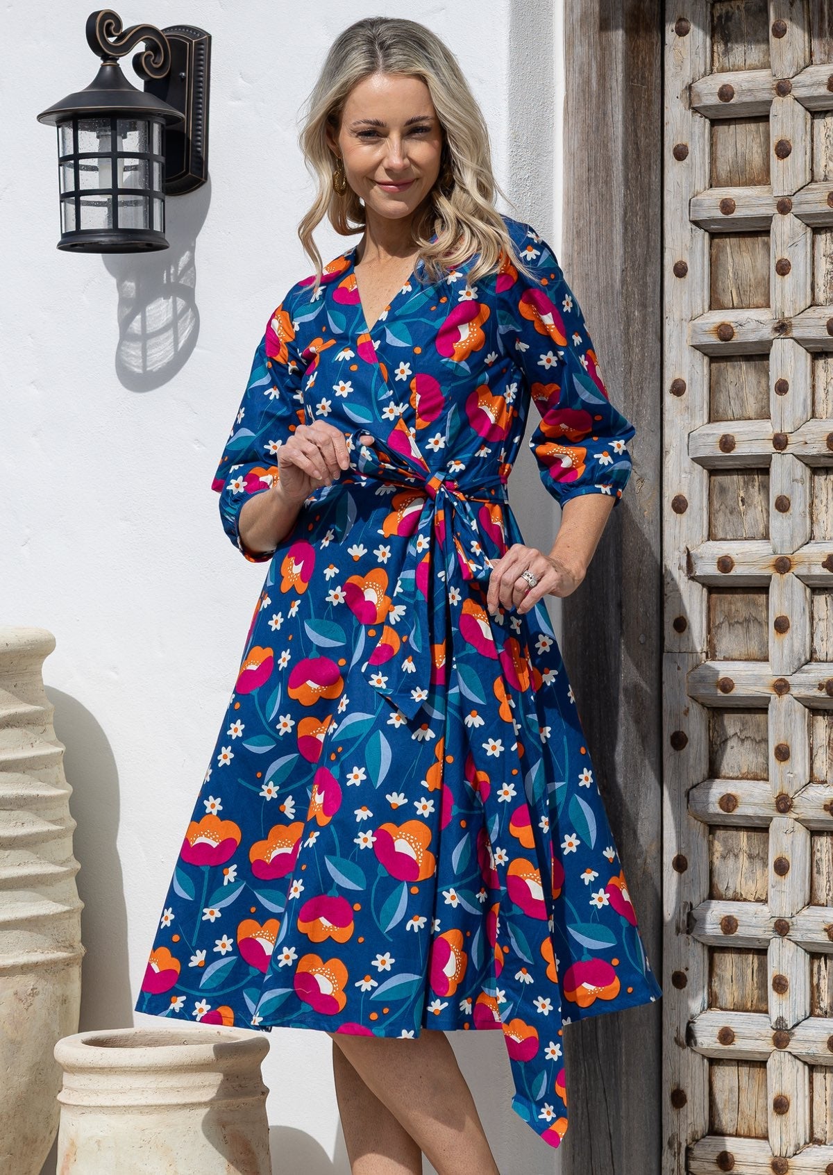 Model wearing 3/4 sleeved royal blue based floral print cotton wrap dress with V-neckline and pockets.