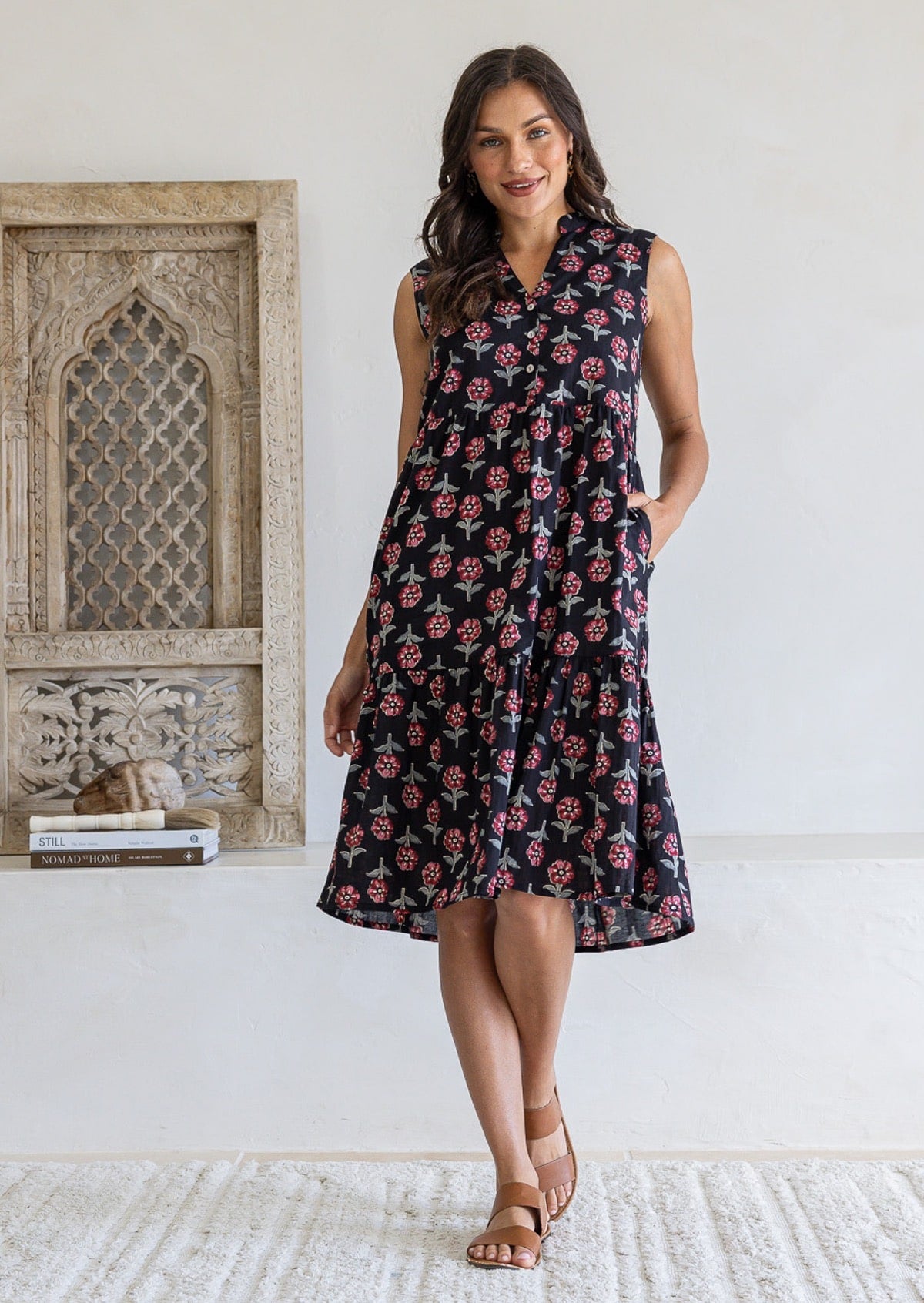 A woman modelling a sleeveless black based floral print cotton midi dress with a one hand in pockets