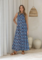 Woman wearing a navy based floral cotton sleeveless button through dress, with high neckline