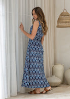 Woman stands sideways wearing a sleeveless button through floral cotton maxi dress with a navy base 