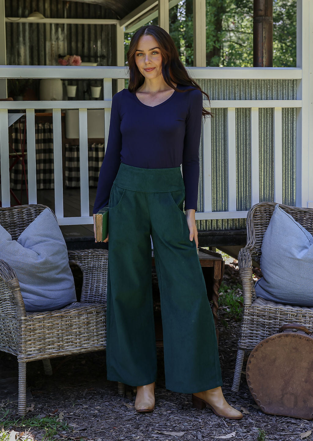 Woman standing on a porch wearing a navy top and green wide-leg pants.