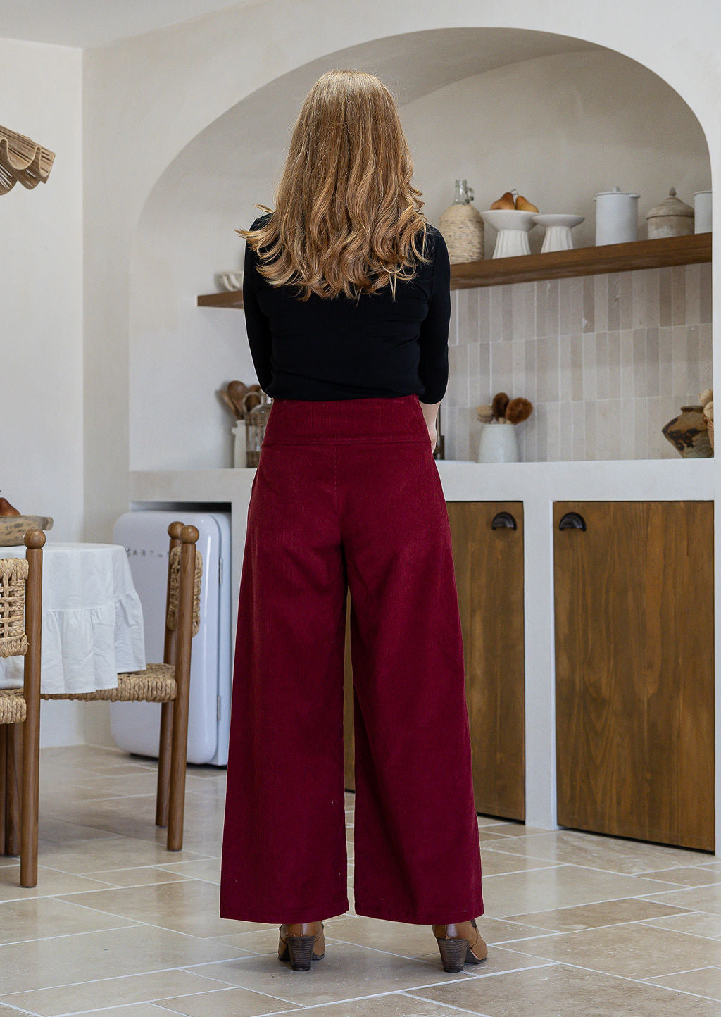 Woman stands backwards wearing a cotton corduroy wide leg pants in deep red with wide waistband and a side zip