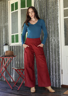 Woman in blue basic top and red cotton corduroy wide leg pants with hands in pockets