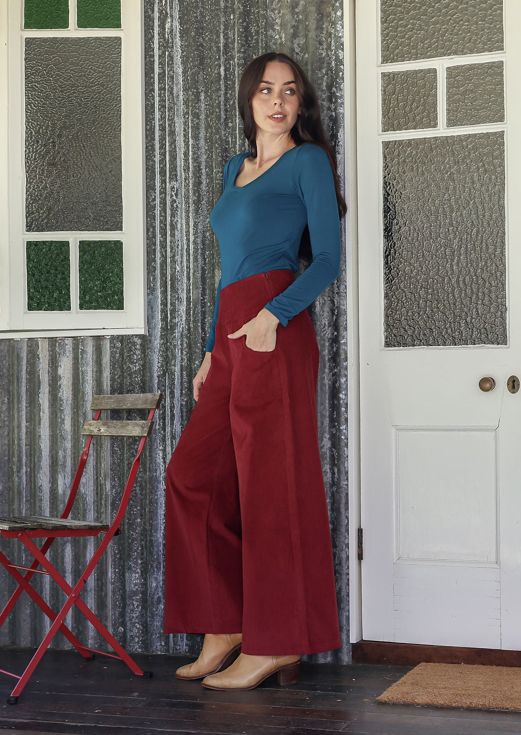 Woman in a red corduroy pants standing in a room with a red chair and white door.
