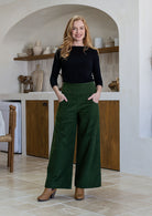 Woman wearing a cotton corduroy wide leg pants in olive green with both hand in pockets paired with a basic black top. 