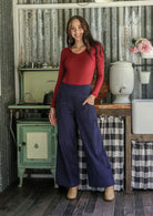 Woman in red long sleeve top and blue cotton corduroy pants standing in a rustic interior setting