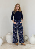Woman wearing a wide leg cotton corduroy pants in navy blue based floral print with both hand in pockets paired with a basic top