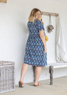 Model stands backwards wearing a cotton V-neck relaxed fit dress with empire waistline and short sleeves.