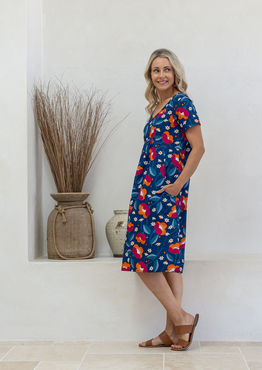 Model stands sideways wearing a cotton V-neck relaxed fit dress with empire waistline and short sleeves.