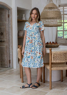 Model wearing a 100% cotton knee length dress with empire waist, short sleeves and pockets in front of dining room table