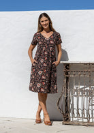 Woman wearing a floral dress standing against a white wall with a metal gate.