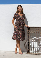 Model wearing a cotton knee length dress with empire waist, short sleeves and one hand in pocket.