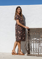 Model stands sideways wearing a cotton V-neck relaxed fit dress with empire waistline and short sleeves.