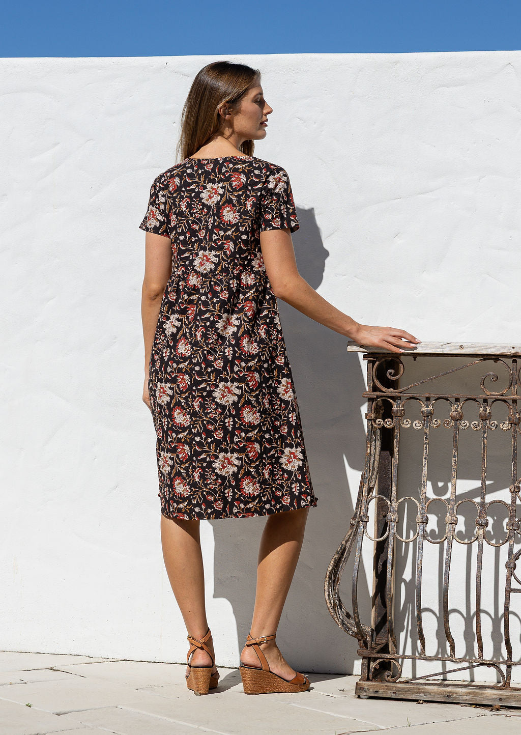 Model stands backwards wearing a cotton V-neck relaxed fit dress with empire waistline and short sleeves.