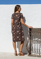 Model stands backwards wearing a cotton V-neck relaxed fit dress with empire waistline and short sleeves.