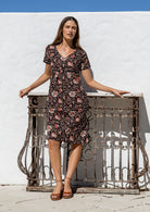 Woman in a floral dress standing against a white wall with a decorative metal railing.