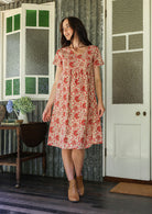 Woman in a floral dress standing in a room with patterned walls and a door.