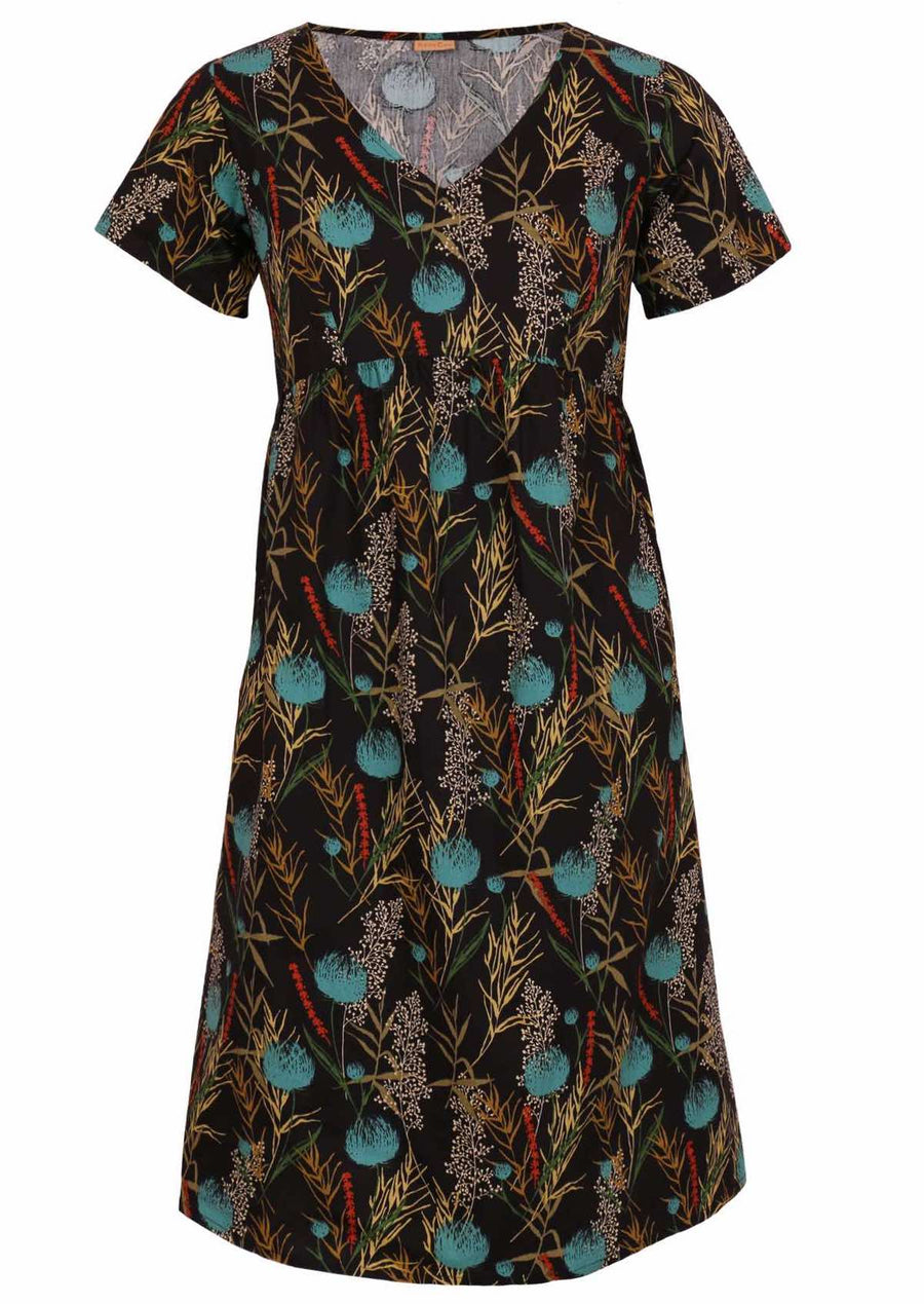 Model wears Etta Dress Thistle V-neck short sleeve below knee length cotton dress with empire waistline in botanical print with black base 