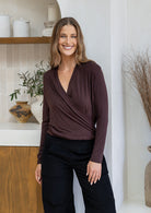 Woman wearing a false wrap front, long sleeve top in dark brown stretch rayon jersey, paired with black pants