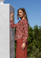 Woman standing sideways wearing a 100% cotton full sleeves top in red based floral print with V neckline