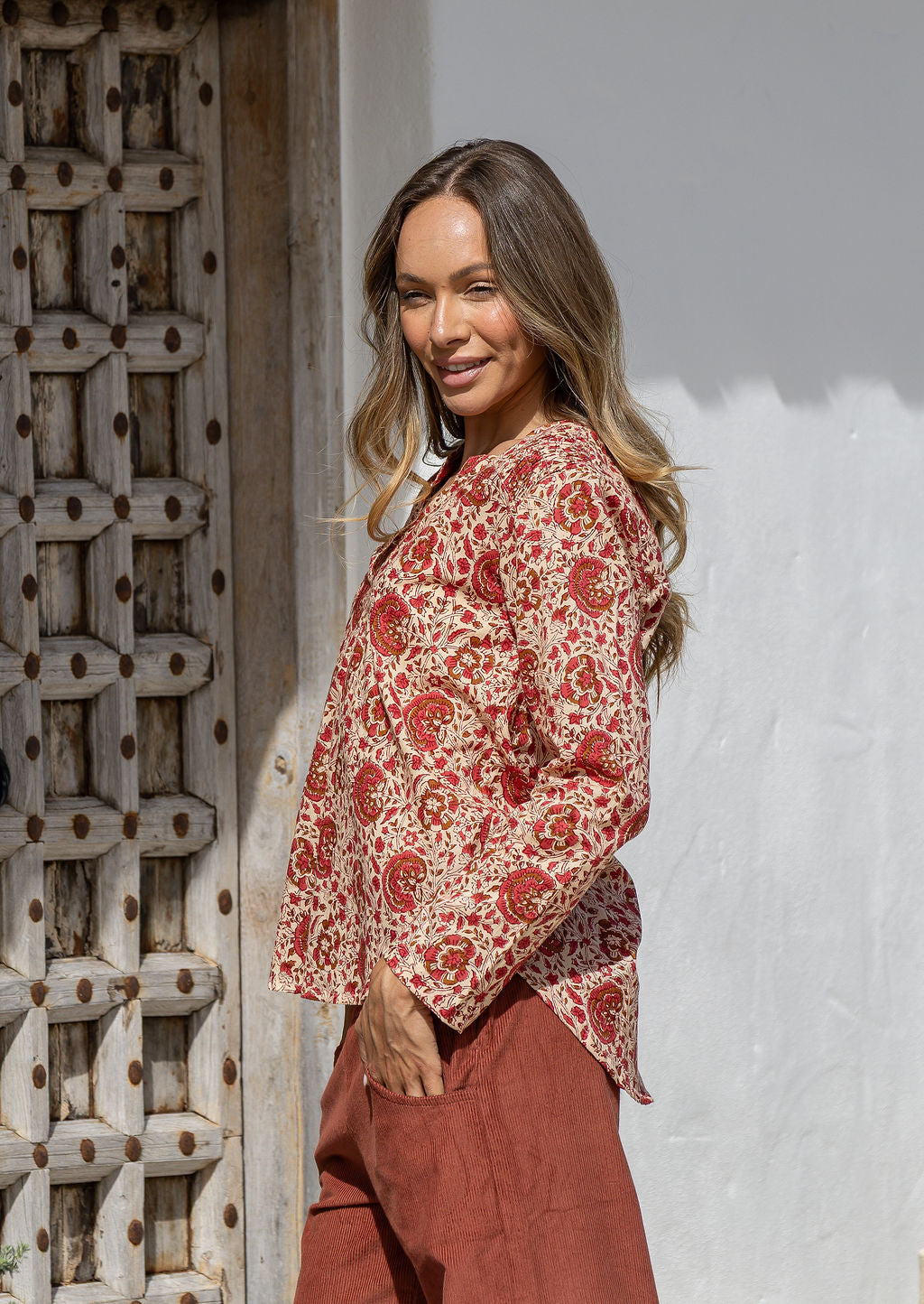 Woman standing sideways wearing a 100% cotton full sleeves top in cream based floral print with V neckline