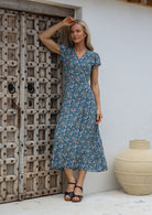 Woman wearing a 100% rayon, blue floral wrap around maxi dress with short cap sleeves and long fabric ties to secure the dress