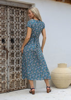 Woman standing in a back pose wearing a 100% rayon wrap dress in blue based floral print with butterfly sleeves and long fabric ties