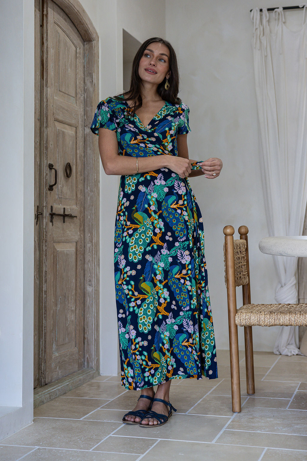 A woman modeling a short-sleeve wrap maxi dress with a navy blue based multicolour floral print. 