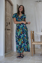 A woman modeling a short-sleeve wrap maxi dress with a navy blue based multicolour floral print. 