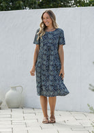 Woman wearing a 100% cotton blue floral dress standing against a white wall.