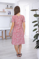 Woman stands backwards wearing a 100% cotton dress in warm pink based floral print 
