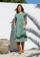 Woman wearing a sage green based floral print cotton dress with hands in pocket