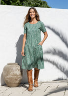 Woman wearing a sage green based floral print cotton dress with one hand in pocket