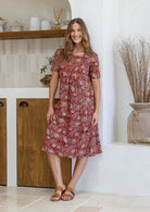 Woman wearing a red floral dress standing in a kitchen.