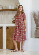 Woman wearing a red based floral print cotton dress with one hand in pocket