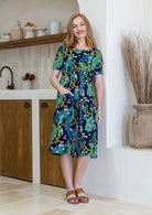 Woman poses in a navy based cotton colourful floral short sleeve dress with round neckline
