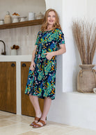woman wearing a 100% cotton dress with one hand in pocket in navy based colourful florals