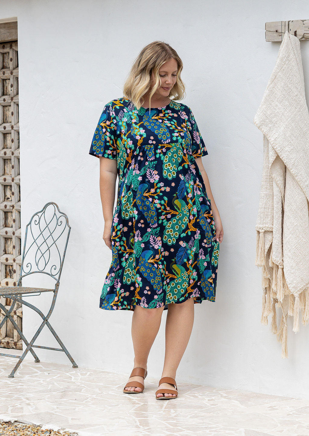 Woman wearing a 100% cotton lightweight lined relaxed fit knee length dress with pin tucks and pockets 