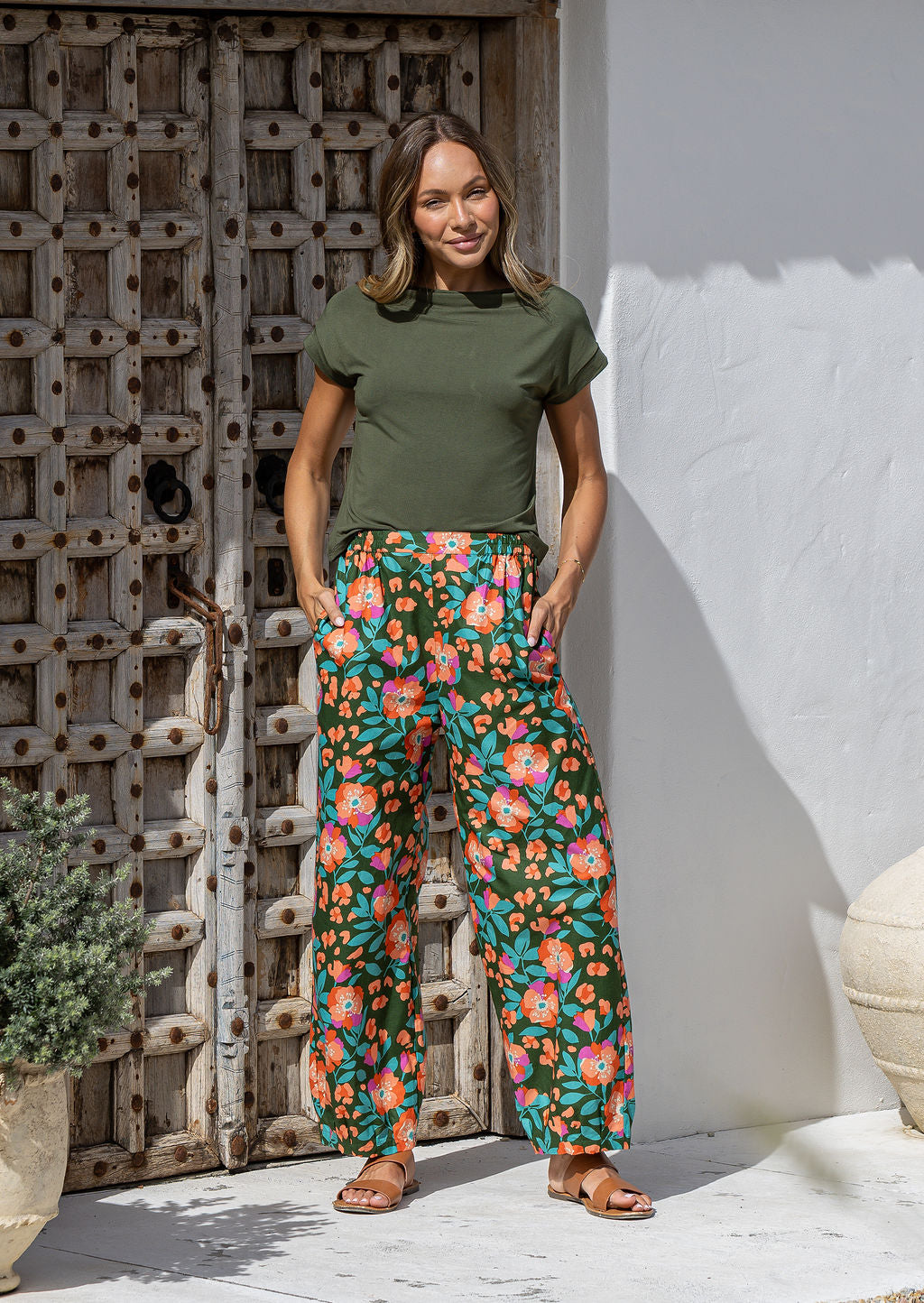 Woman wearing a basic top and wide leg cotton pants in olive green based floral print with both hand in pockets.