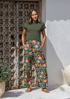 Woman wearing a basic top and wide leg cotton pants in olive green based floral print with both hand in pockets.