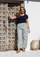 Woman wearing a navy blue t-shirt with round neck and white floral cotton pants in front of old wooden door