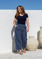 Woman wearing a 100% cotton wide leg pants in navy based white striped print with pockets and pleats at the ankle.