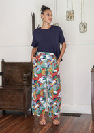 Woman wearing a basic top and colourful floral cotton pants with hand in pockets standing in a decorative indoor setting. 