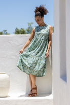 Model wears 100% cotton sleeveless midi dress with high round neckline, tiered design and pockets in sage green based  floral print