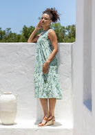 Woman stands sideways wearing a sleeveless cotton midi dress with two tiered design and high round neckline